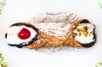 top view of typical sicilian pastry Cannolo sprinkled with confectioner's sugar on white plate