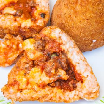 traditional sicilian street food - open meat ragu stuffed rice balls arancini on plate