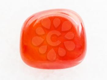 macro shooting of natural mineral rock specimen - tumbled carnelian gem on white marble background