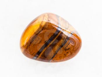 macro shooting of natural mineral rock specimen - tumbled tigers eye gem stone on white marble background