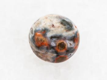 macro shooting of natural mineral rock specimen - tumbled orbicular jasper gemstone on white marble background