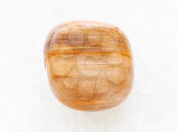 macro shooting of natural mineral rock specimen - polished brown tiger's eye gem on white marble background