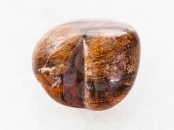 macro shooting of natural mineral rock specimen - tumbled tiger-eye stone on white marble background