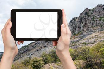 travel concept - tourist photographs old rocks at Demerdzhi (Demirci) Mountain from The Valley of Ghosts on Crimean Southern Coast in september on tablet with cut out screen for advertising logo