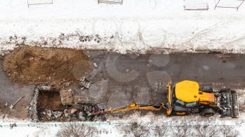 above view of tractor digging road to change sewer pipes in winter in Moscow city