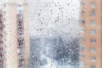 urban background - rain drops on home window glass (focus on water trickles on windowpane) in winter season