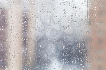 urban background - rain drops on window glass (focus on water trickles on windowpane) in winter day