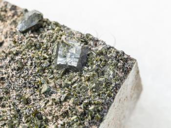 macro shooting of natural mineral stone specimen - crystals of Epidote close up on stone on white marble background from Irkutsk region, Russia