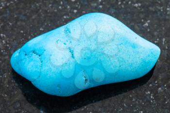 macro shooting of natural mineral rock specimen - polished Turquenite (blue howlite) gemstone on dark granite background