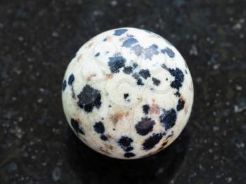 macro shooting of natural mineral rock specimen - ball from Dalmatian Jasper gemstone on dark granite background