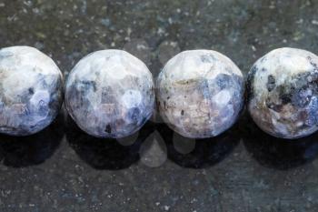 macro shooting of natural mineral rock specimen - necklace from gray Labradorite gemstone on dark granite background