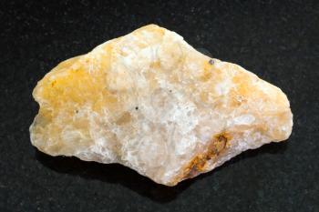 macro shooting of natural mineral rock specimen - pebble of yellow Calcite stone on dark granite background