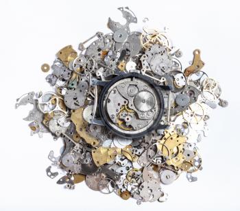 watchmaker workshop - top view of open mechanical watch on pile of old clock spare parts on white background