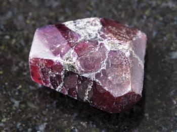 macro shooting of natural mineral rock specimen - raw crystal of red garnet gemstone on dark granite background