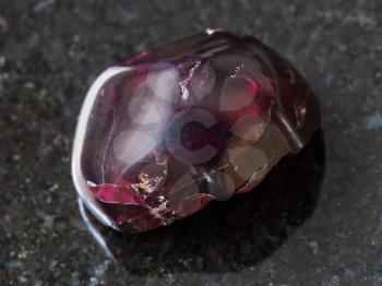 macro shooting of natural mineral rock specimen - tumbled red garnet gemstone on dark granite background