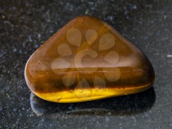 macro shooting of natural mineral rock specimen - tumbled tiger-eye gem stone on dark granite background from South Africa
