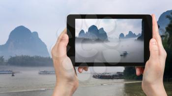 travel concept - tourist photographs boats in mist on river near Xingping town in Yangshuo county in spring morning in China on tablet