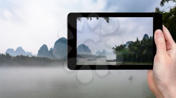 travel concept - tourist photographs fog over river near Xingping town in Yangshuo county in spring morning in China on tablet