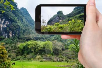 travel concept - tourist photographs overgrown rocks of karst mountains in Yangshuo County in spring season in China on smartphone