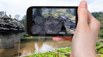 travel concept - tourist photographs village houses near Chengyang Wind and Rain (Fengyu, Yongji, Panlong) Bridge in Sanjiang Dong Autonomous County in China in spring on smartphone