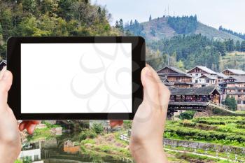 travel concept - tourist photographs country houses and Wind and Rain (Fengyu) bridge in Chengyang village of Sanjiang Dong Autonomous County in China on tablet with cut out screen for advertising