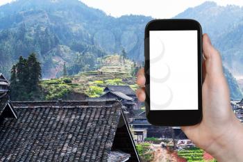travel concept - tourist photographs country houses of Chengyang village of Sanjiang Dong Autonomous County in China in spring on smartphone with cut out screen for advertising
