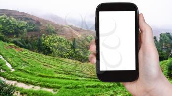 travel concept - tourist photographs wet Rice Terraces from Tiantouzhai village in Dazhai Longsheng (Dragon's Backbone, Longji) county in spring on smartphone with cut out screen for advertising logo