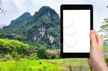 travel concept - tourist photographs karst mountain in Yangshuo County in China in spring season on tablet with cut out screen for advertising logo