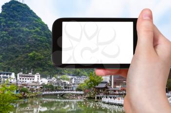 travel concept - tourist photograps Yangshuo town in China in spring on smartphone with cut out screen for advertising logo