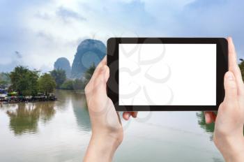 travel concept - tourist photographs calm surface Yulong and Jinbao rivers and karst peaks in Yangshuo County in China in spring on tablet with cut out screen for advertising logo