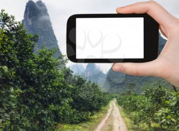 travel concept - tourist photograps country road to karst peaks in Yangshuo County in China in spring season on smartphone with cut out screen for advertising logo