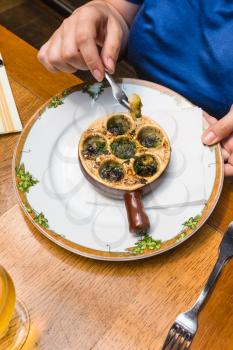 travel to France - woman eats snails in burgundy style (escargots a la bourguignonne) in restaurant in Etretat town in Normandy