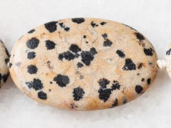 macro shooting of natural mineral rock specimen - bead from Dalmatian Jasper gemstone on white marble background