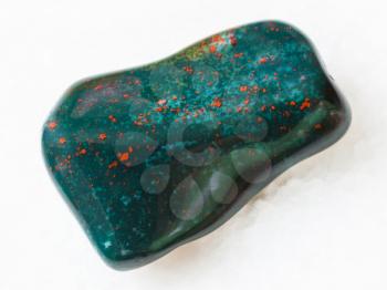 macro shooting of natural mineral rock specimen - tumbled green Heliotrope (bloodstone) gem stone on white marble background from India