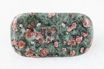 macro shooting of natural mineral rock specimen - polished Eclogite gemstone on white marble background from Salma region, Kola peninsula, Russia