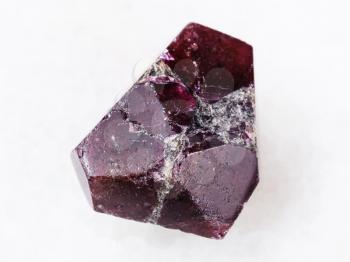 macro shooting of natural mineral rock specimen - raw crystal of red garnet gemstone on white marble background