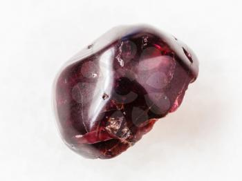macro shooting of natural mineral rock specimen - tumbled red garnet gemstone on white marble background