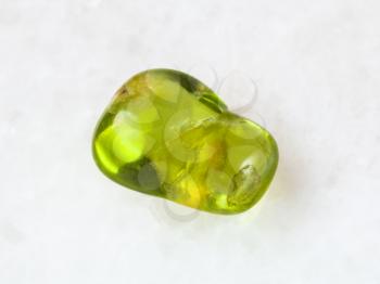 macro shooting of natural mineral rock specimen - tumbled olivine gem stone on white marble background from Pakistan