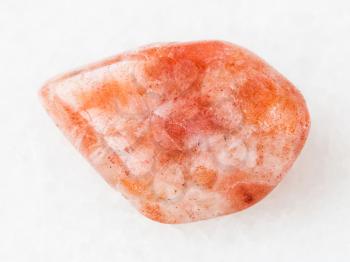 macro shooting of natural mineral rock specimen - tumbled sunstone (heliolite) gemstone on white marble background from USA
