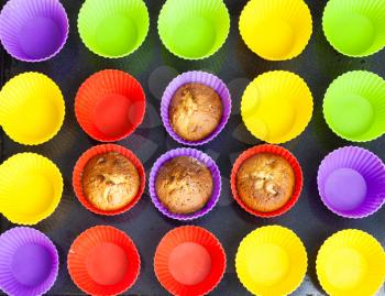 top view of four baked cupcakes and many empty multicolored silicone molds on dark tray