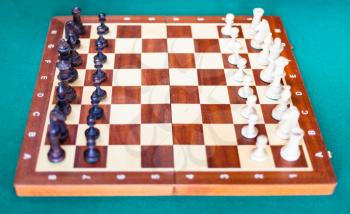 wooden chessboard with chess pieces in starting position on green baize table. Focus on the middle of the board