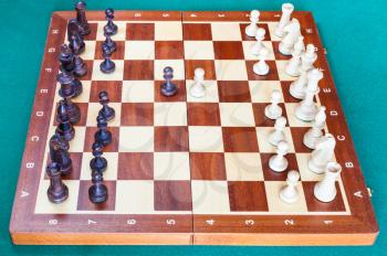 side view of wooden chessboard with first chess pawn moves on green baize table