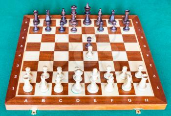 view from white side of wooden chessboard with first chess pawn moves on green baize table