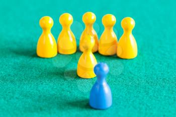 concept scene - yellow pawns with leader in front of one blue pawn on green baize table. Focus on yellow leader