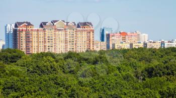 panoramic view of green city park and apartment houses illuminated by sun in sunny summer day