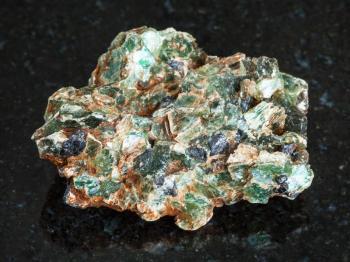 macro shooting of natural mineral - green beryl and emerald crystals in raw rock on black granite from Ural Mountains