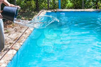 man pours of disinfectant from bucket in outdoor swimming pool on backyard of country house