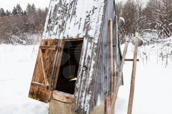open well at the edge of the forest in russian village with old typical tools (ice picks and ladles) in overcast winter day in Smolensk region of Russia