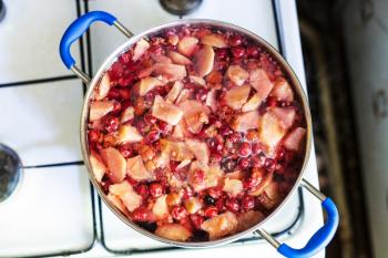 top view of cooking of local non-alcoholic sweet beverage Kompot (compote) from fresh apricot fruits, raspberries, cherries in rural kitchen
