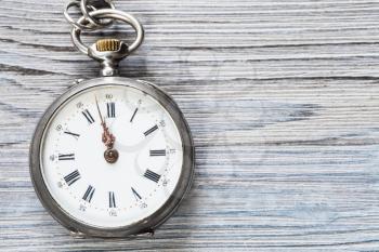two minutes to twelve o'clock on vintage pocket watch on gray wooden background